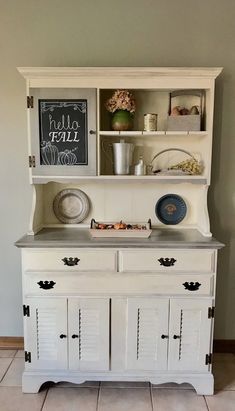 an old dresser is painted white and has some plates on the top, with flowers in vases