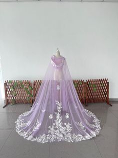 a purple wedding dress with white flowers on it and a veil hanging from the back