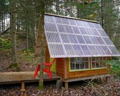 a small wooden cabin with a solar panel on the roof and red chair in front