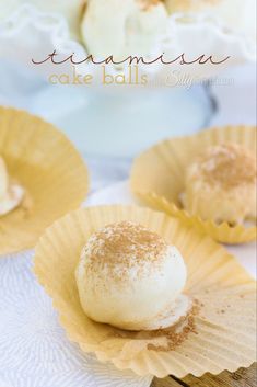 some desserts are sitting in paper cups on a white tablecloth and there is a plate with cake balls next to it