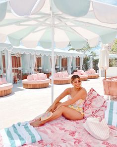 a woman sitting on top of a pink and white bed covered in sun shade umbrellas