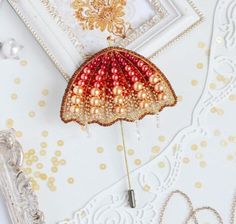 a red and gold brooch sitting on top of a table next to a white frame