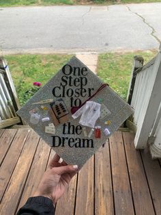 someone holding up a graduation cap that says one step closer to the dream