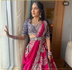 a woman in a pink and blue lehenga standing next to a window with her hands out