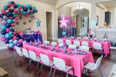 a room filled with lots of tables covered in pink and blue balloons next to a star shaped arch