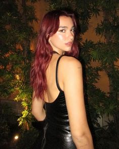 a woman with long red hair wearing a black leather dress and looking at the camera