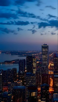 an aerial view of the city lights and skyscrapers at night, with water in the background