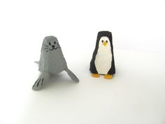 two small stuffed animals sitting next to each other on a white surface, one penguin and the other seal