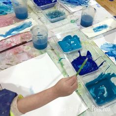 the child is painting with blue paint on paper