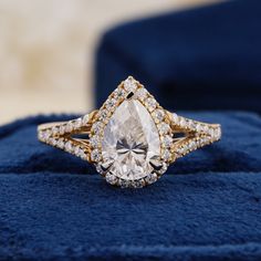 an engagement ring with a pear shaped diamond surrounded by smaller round diamonds on a blue velvet cushion