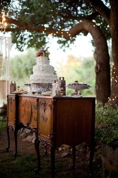 a table that has a cake on it and lights hanging from the trees in the background