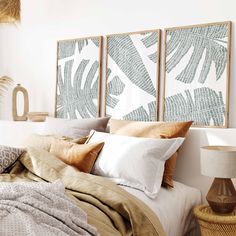 a bed with pillows and blankets on top of it next to two pictures hanging above the headboard