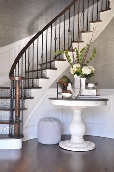 a white table sitting under a stair case next to a bannister with flowers on it