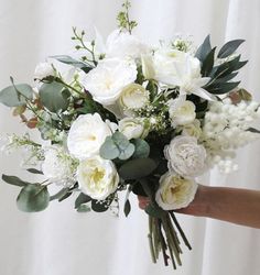 a person holding a bouquet of white flowers in their hand with greenery on the side