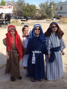 three children dressed up in costumes standing next to each other on a dirt road with an rv in the background