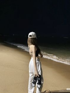 a woman standing on top of a sandy beach next to the ocean at night time