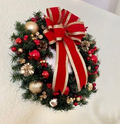 a christmas wreath with red and gold ornaments on it, hanging from the side of a wall