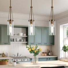 three lights hanging over a kitchen island with flowers in vases on the counter top