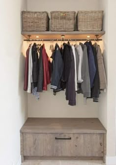 an organized closet with clothes and baskets hanging on the wall next to a wooden bench