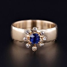 a gold ring with an oval blue sapphire surrounded by small white and yellow diamonds on a black background