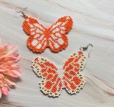 two orange and white beaded butterfly earrings next to a pink flower