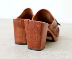 "1970s Leather and wood wedges in size 5-1/2. Slip on style with full leather lining. Squared toe and contrast stitching in dark brown. Buckle detail. Perforated pattern. Genuine wood heel and soles. Genuine leather in an antiqued cognac color. In excellent vintage condition with just one split in the wood heel (this does not seem to be a stability issue for the shoes). Brand: Thom McAn // Woodworks Made in Brazil Size: None Listed; Recommending a size 5-1/2. FOR REFERENCE: I wear a size 6-1/2 t Retro Brown Leather Clogs, Vintage Brown High Heel Clogs, Vintage Clogs With Stacked Heel For Spring, Vintage Spring Clogs With Stacked Heel, Vintage Leather Clogs For Spring, Vintage Brown Closed Toe Clogs, Retro Brown Closed Toe Clogs, Vintage Brown Open Toe Clogs, Leather And Wood