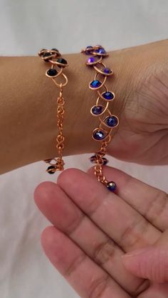 a person is holding two bracelets on their arm, one with blue beads and the other with gold chains