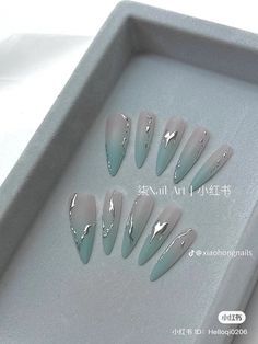 six fake nails in a tray on a white surface with silver foil and black tips