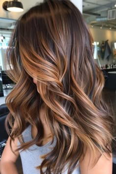 Woman with long, wavy, brunette hair featuring caramel highlights in a modern salon. Fall Balayage Brunette Honey, Copper Lowlights On Light Brown Hair, Highlights Brown Hair Blonde Honey Caramel, Caramel Honey Highlights On Dark Hair, Reddish Brown Hair With Highlights Caramel Red, Toffee Brown Hair Color, Lowlights On Brown Hair, Toffee Brown Hair, Toffee Balayage