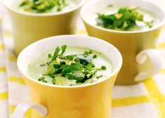 three yellow cups filled with soup and garnished with green herbs on a checkered table cloth