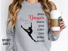 a woman holding a cup of coffee and wearing a dance sweatshirt