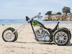 a green and black motorcycle parked on top of a sandy beach