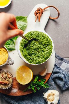 a person spooning pesto into a bowl with lemons, garlic and parsley