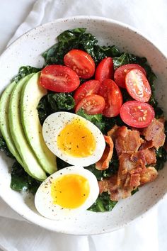 a white bowl filled with bacon, avocado and hard boiled eggs on top of spinach