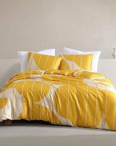 a bed with yellow and white comforters in a room next to a lamp on the wall