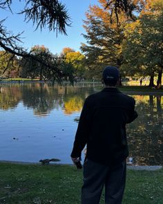 a man standing in front of a body of water with trees around him and ducks on the ground