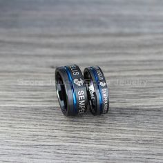 two black and blue wedding rings with the words sern written on each ring, sitting on top of a wooden table