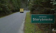 a green street sign sitting on the side of a road next to a lush green forest