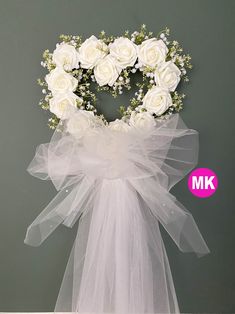 white roses arranged in a heart shaped wreath on top of a veiled chair rail