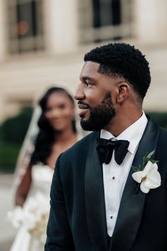 a man in a tuxedo looks off into the distance as he stands next to his bride