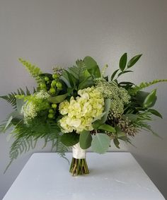 a vase filled with green flowers and greenery on top of a white countertop