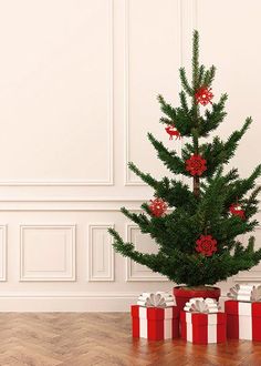 a small christmas tree with red and white presents under it on a wooden floor in front of a wall