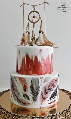 a three tiered cake decorated with feathers and dream catchers on it's top