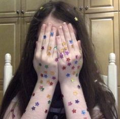 a girl with stars painted on her hands covering her face