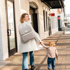 a woman holding the hand of a small child walking down a sidewalk in front of a building