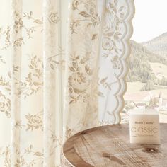 a wooden table sitting in front of a window next to a pair of white curtains