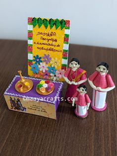 two small figurines are standing next to a greeting card on a wooden table