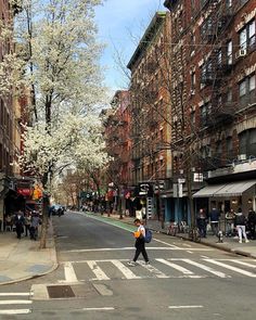 a person walking across a street in front of tall buildings with white flowers on them