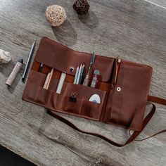 a brown leather bag with pens, pencils and other items in it on a table