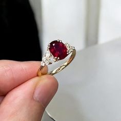 a person holding a ring with a red stone in it's center and two white diamonds around the band